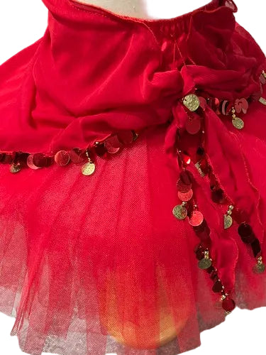 A close-up of a bright red tulle tutu skirt with a gathered waistband and dangling red sequins and gold coin charms, displayed on a mannequin against a gray floor and white wall.