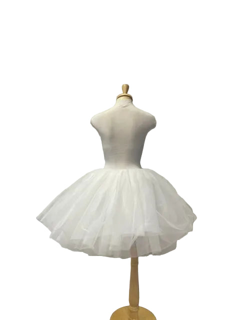 A white tulle tutu dress displayed on a cream mannequin torso with a wooden stand, set against a white shiplap wall in a boutique interior.