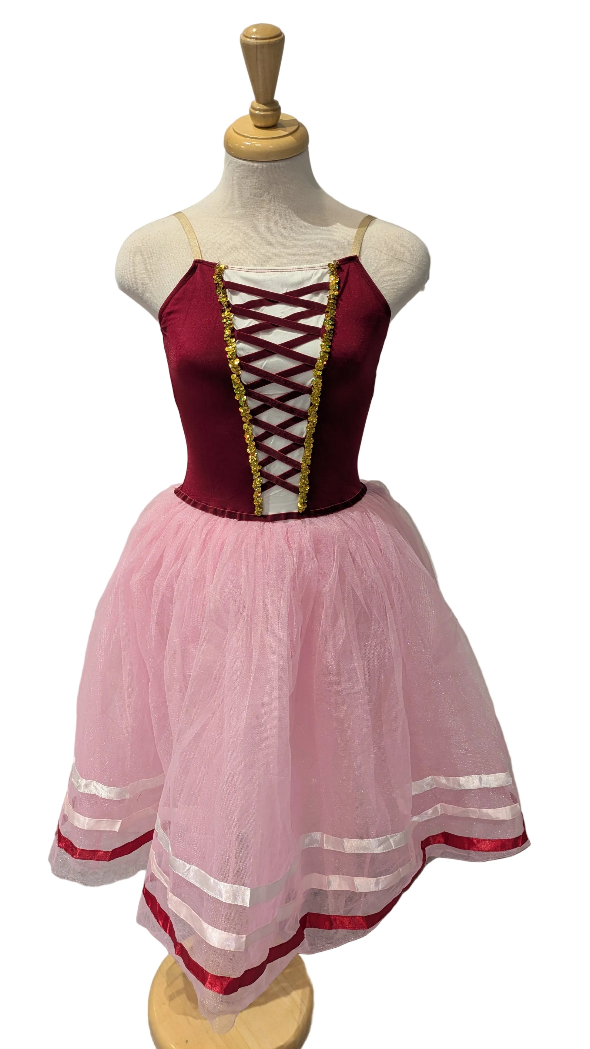 A children's costume dress displayed on a mannequin, featuring a deep burgundy corset-style bodice with gold trim and lace-up detailing, paired with a voluminous light pink tulle skirt trimmed with red and white stripes.