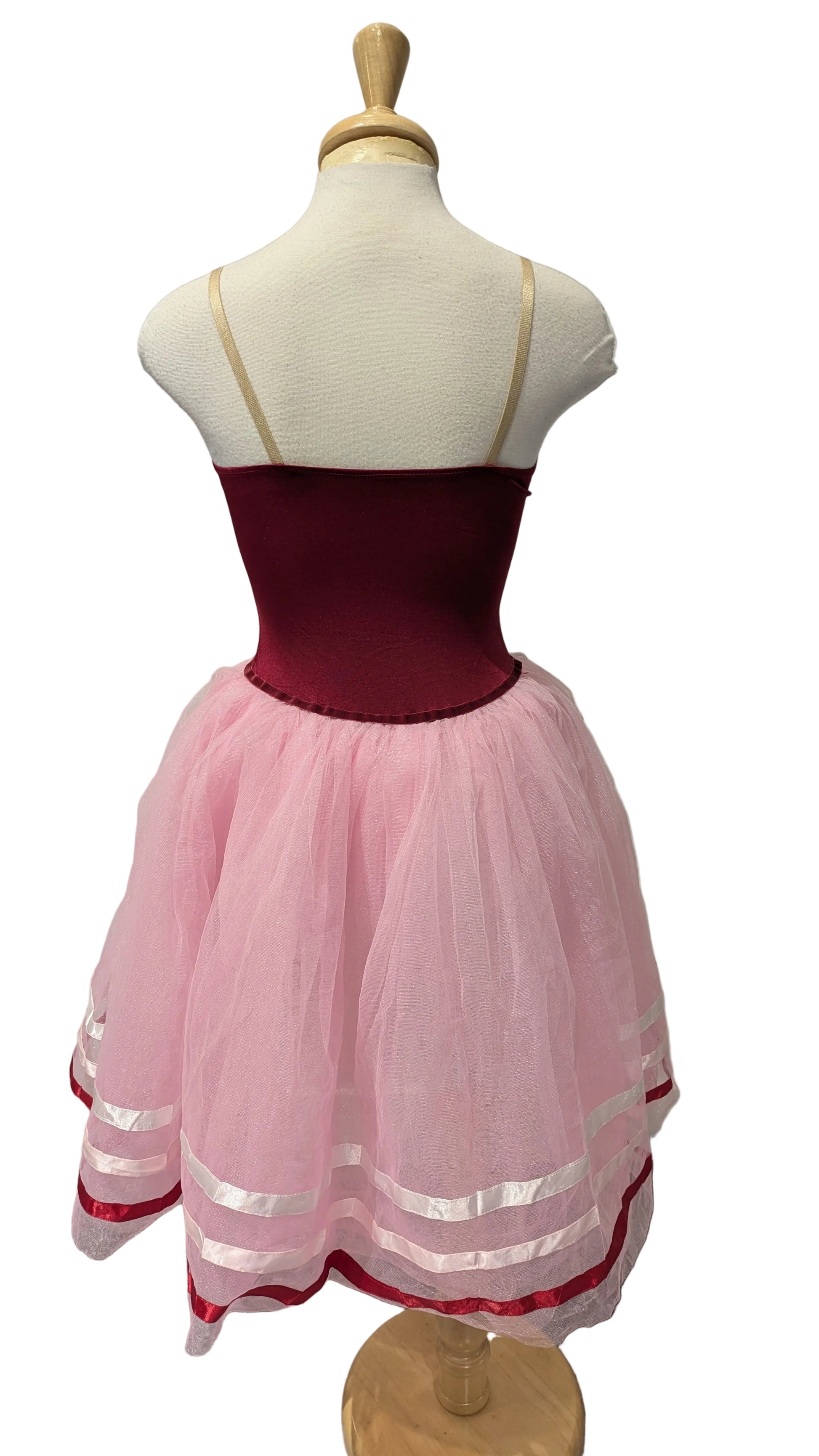 A children's dress displayed on a mannequin, featuring a deep burgundy corset-style bodice with thin beige straps and a voluminous light pink tulle skirt with white horizontal stripes near the hem.
