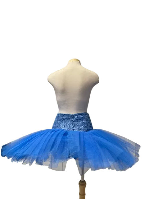 A bright blue tutu skirt with a sparkly blue waistband displayed on a white mannequin torso in front of a white paneled door.