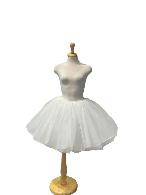 A white tulle tutu dress displayed on a mannequin torso in a boutique setting with a white paneled wall and gray floor.