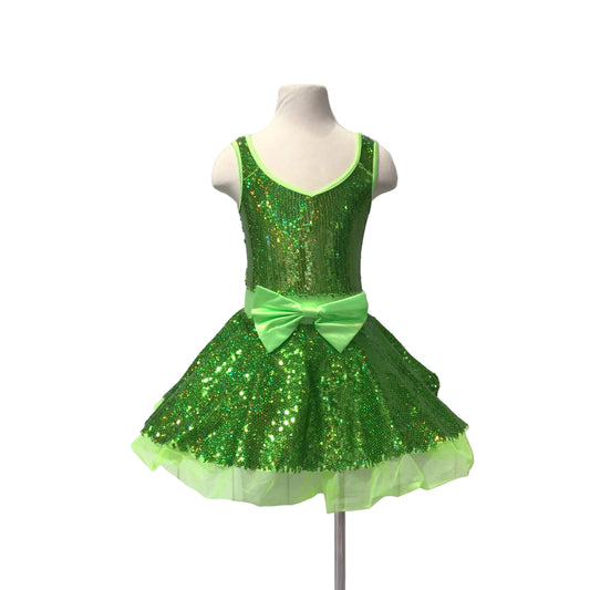 A green sequined dance dress displayed on a white mannequin torso against a white paneled wall. The dress features a sleeveless bodice, a ruffled tutu skirt, and a large green bow at the waist.