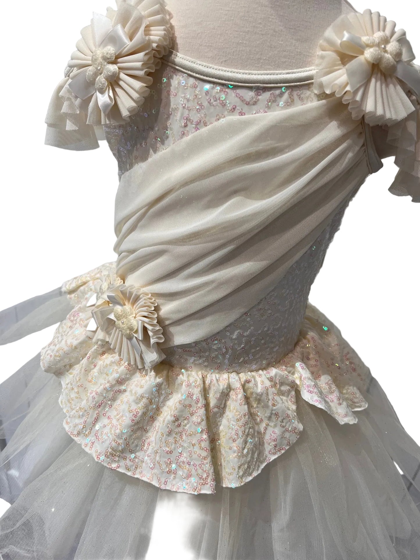 A cream-colored formal party dress displayed on a dress form. The dress features a sheer tulle skirt, a ruffled waistband with a floral applique, a sequined bodice, and a draped satin sash with matching fabric bows on the shoulders.