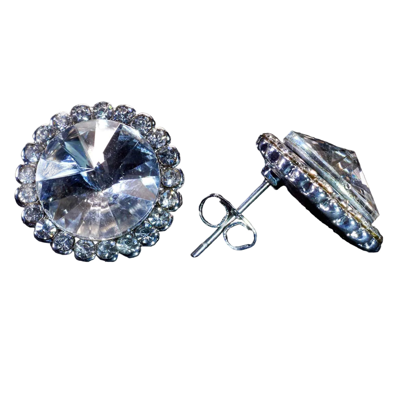 A pair of round halo stud earrings featuring large clear faceted center stones surrounded by a border of smaller clear stones, shown on a dark textured background. One earring is facing forward, and the other is angled to show the post and backing.