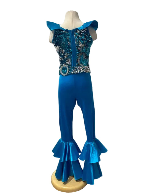 A bright blue and turquoise dance or performance costume displayed on a mannequin. The costume features an off-the-shoulder top with a heavily embellished sequined bodice, matching flared pants, and dramatic ruffled hems, set against a white paneled wall.
