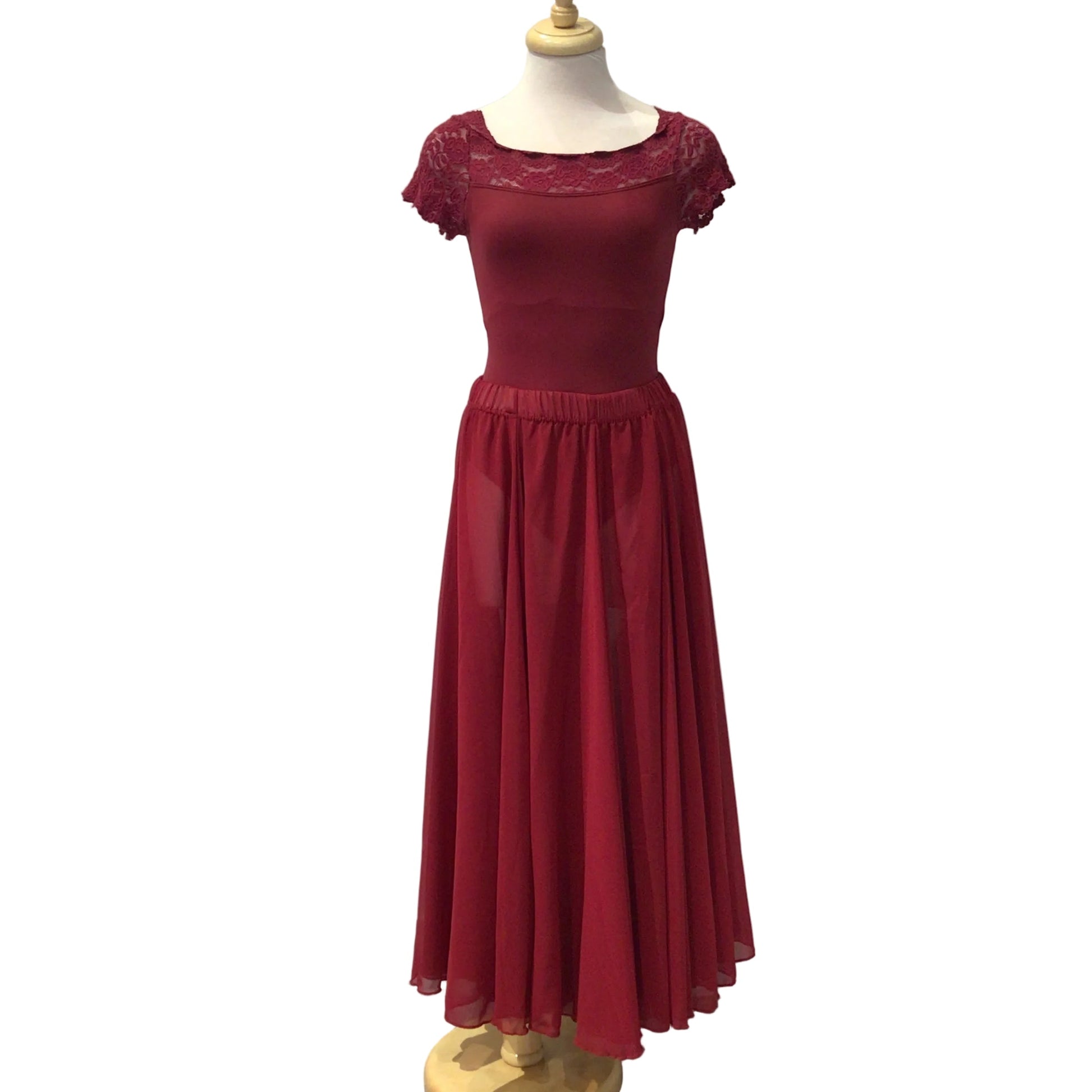 A long red formal gown displayed on a mannequin torso against a white paneled wall, with a gray floor visible at the right edge.