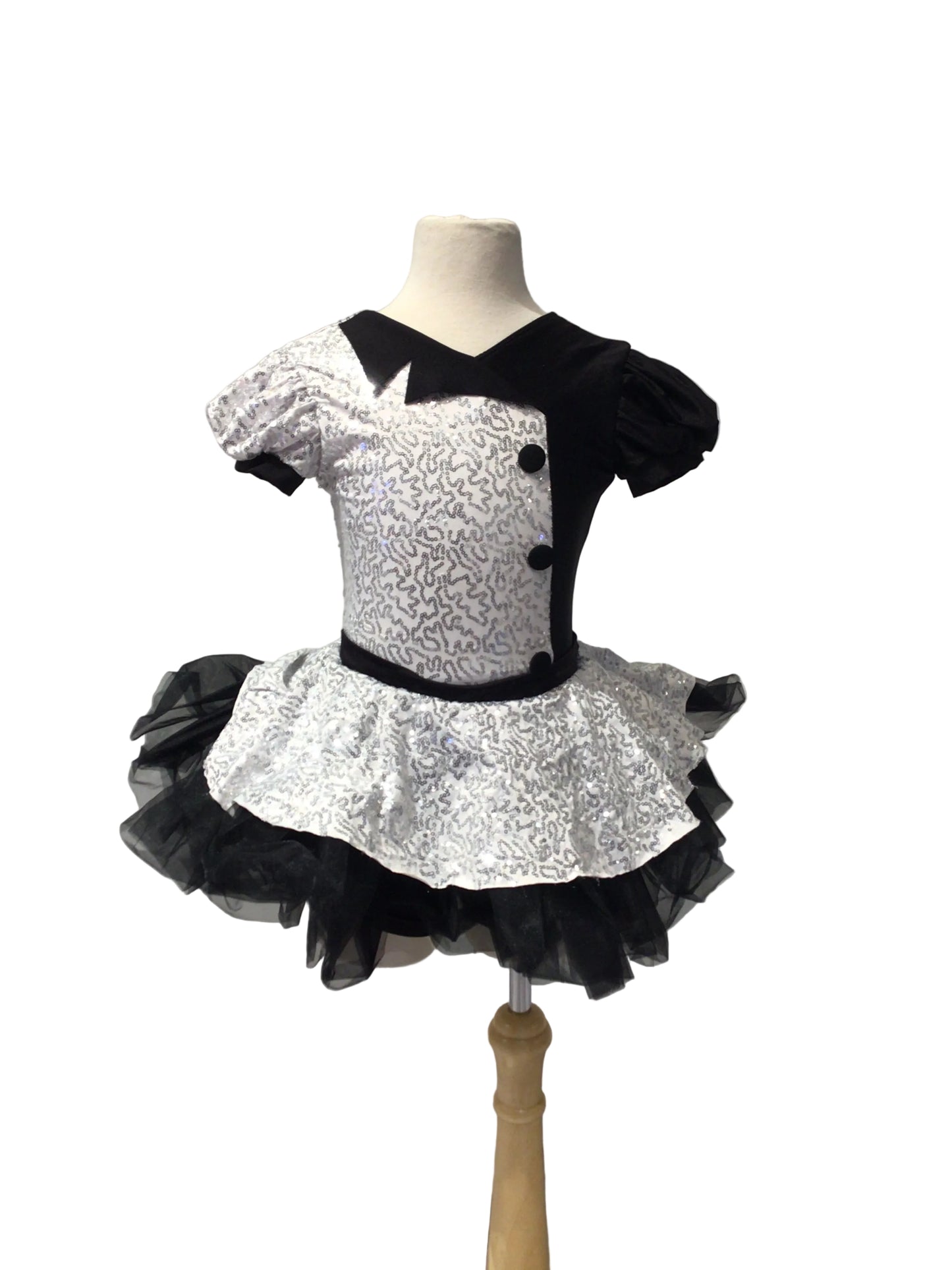 A children's black and white costume dress displayed on a mannequin torso. The dress has a black yoke with three black buttons, a black-and-white patterned bodice, short puff sleeves, a black waistband, and a layered black tulle tutu skirt.