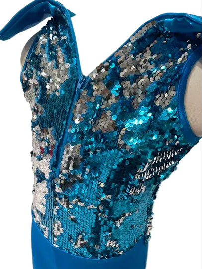A close-up of a bright blue sequined sleeveless top or dress section displayed on a mannequin torso, with matching blue fabric below, photographed indoors against a white paneled wall.