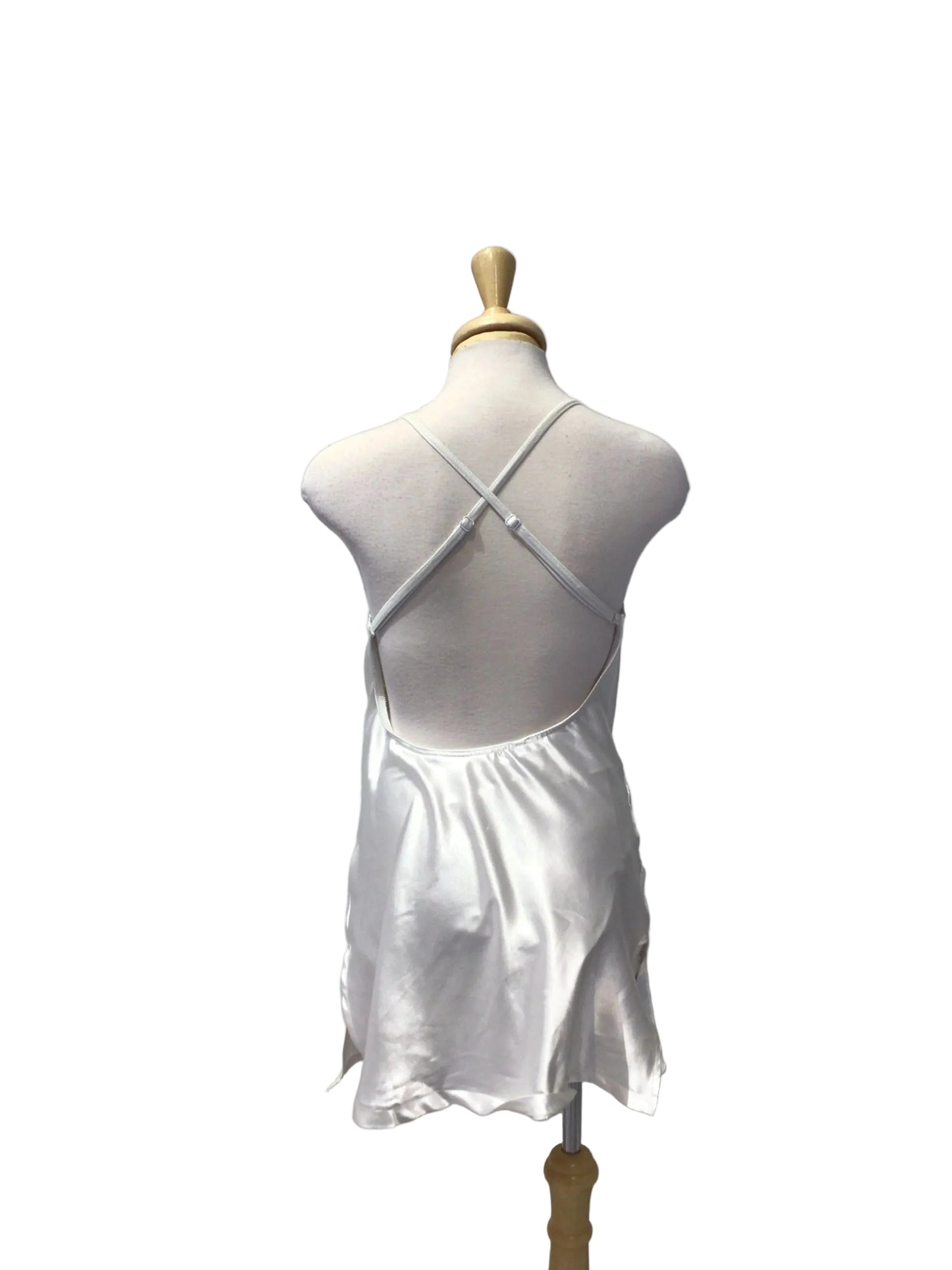 A white satin slip dress displayed on a light gray dress form mannequin, set against a white paneled wall background.
